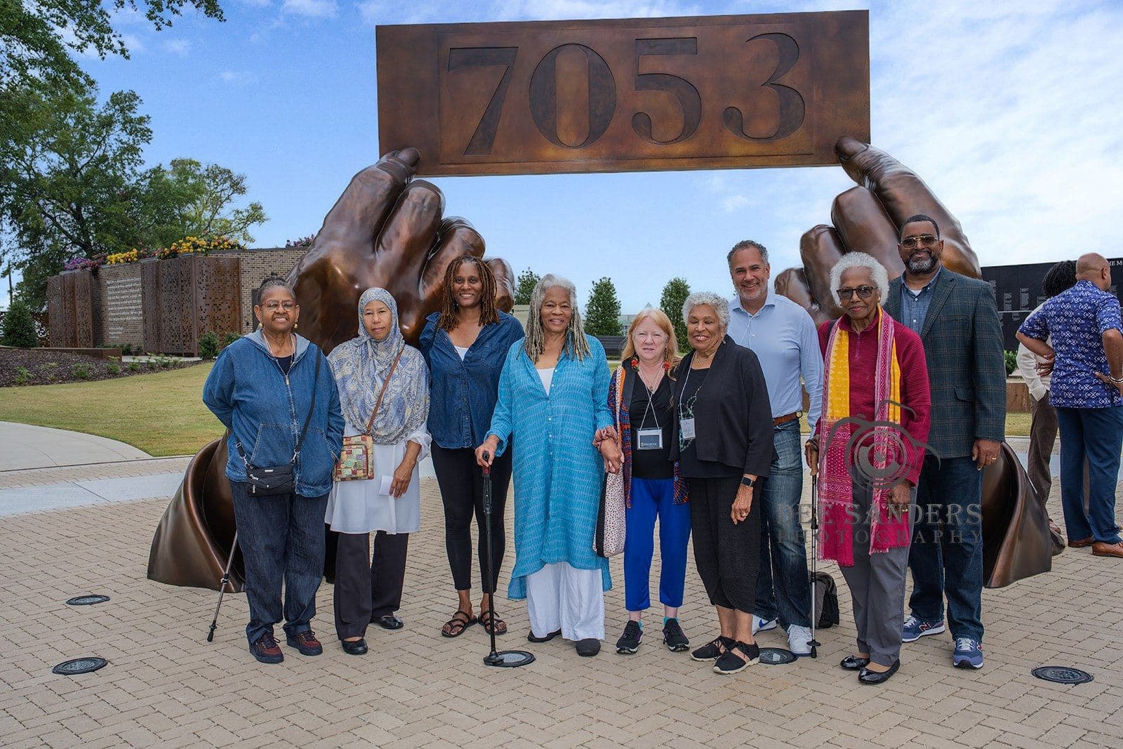 A group of attendees beneath the sculpture of hands holding the number 7053